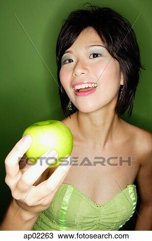 Stock Image - Woman holding green apple towards camera . Fotosearch