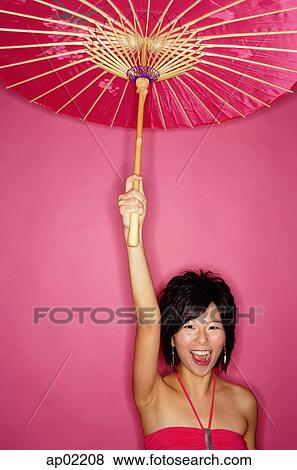 Stock Photo - Woman holding pink umbrella, standing against pink background . Fotosearch
