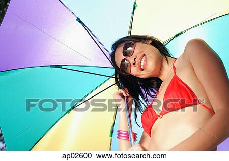 Woman in bikini and sunglasses, holding multi-coloured umbrella, smiling View Large Photo Image Stock Image - Woman in bikini and sunglasses, holding multi-coloured umbrella, smiling . Fotosearch