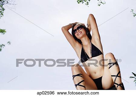 Woman in bikini, sitting, hands behind head, smiling View Large Photo Image Stock Photograph - Woman in bikini, sitting, hands behind head, smiling . Fotosearch
