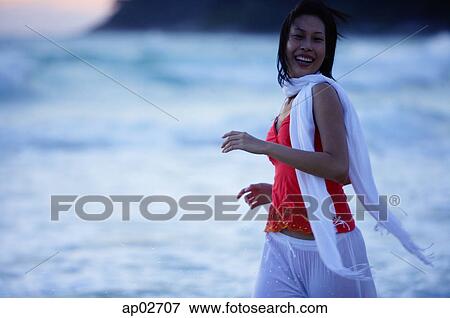Stock Photo - Woman in red top and white scarf, running along beach, smiling. Fotosearch