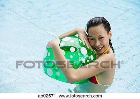 Stock Image - Woman in swimming pool, hugging beach ball, smiling . Fotosearch