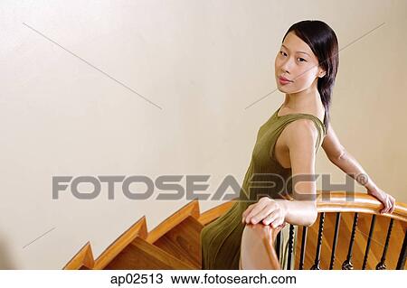 Stock Image - Woman leaning on staircase, looking at camera . Fotosearch