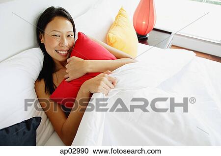 Woman lying in bed, hugging pillow, looking at camera View Large Photo Image Stock Image - Woman lying in bed, hugging pillow, looking at camera . Fotosearch