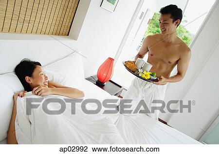 Woman lying in bed, man holding breakfast tray View Large Photo Image Stock Image - Woman lying in bed, man holding breakfast tray . Fotosearch