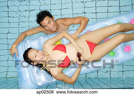 Stock Photo - Woman lying on pool raft, man in water next to her, looking up at camera . Fotosearch