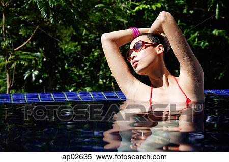 Stock Photography - Woman sitting in swimming pool, hands on head. Fotosearch