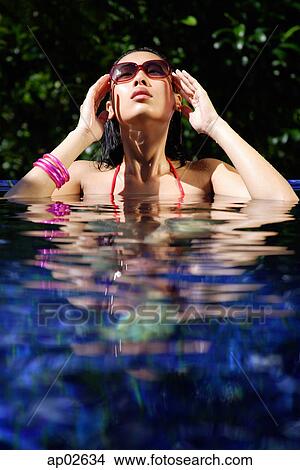 Woman sitting in swimming pool, touching sunglasses View Large Photo Image Picture - Woman sitting in swimming pool, touching sunglasses . Fotosearch