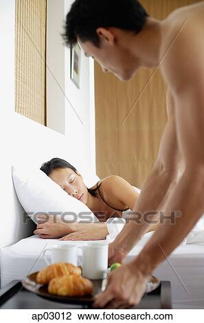 Woman sleeping in bed, man setting down breakfast tray next to her on bedside table View Large Photo Image Stock Image - Woman sleeping in bed, man setting down breakfast tray next to her on bedside table . Fotosearch