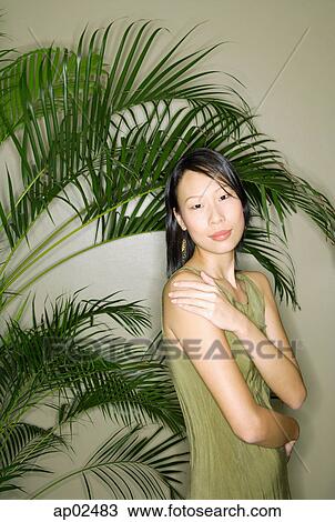 Stock Image - Woman standing next to plant, looking at camera, hand on shoulder . Fotosearch