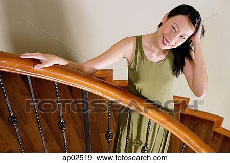 Woman standing on staircase, hand on head, smiling View Large Photo Image Stock Photo - Woman standing on staircase, hand on head, smiling. Fotosearch