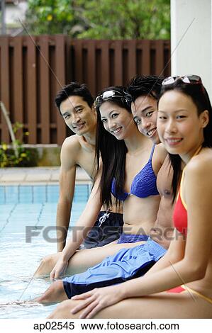 Stock Photography - Young adult couples sitting at edge of swimming pool . Fotosearch