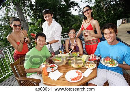 Stock Image - Young adults having a meal on patio, smiling at camera . Fotosearch
