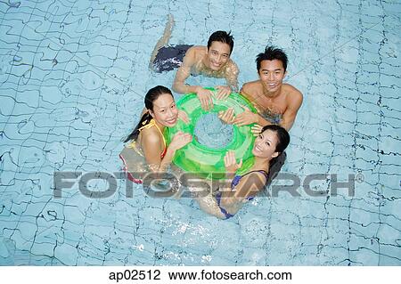 Stock Image - Young adults in swimming pool holding on to inflatable ring. Fotosearch