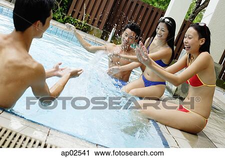 Stock Image - Young adults in swimming pool, splashing water on each other . Fotosearch