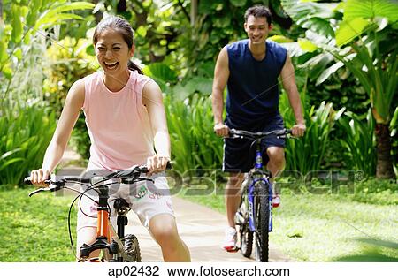 Young couple cycling through a park View Large Photo Image Stock Image - Young couple cycling through a park. Fotosearch