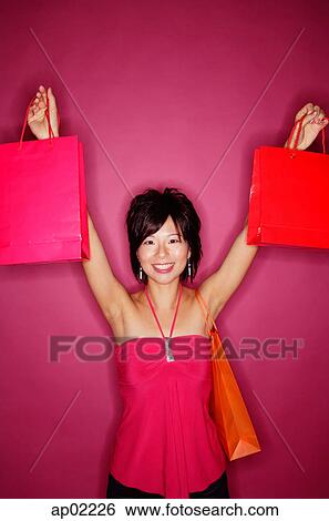 Young woman against pink background holding up shopping bags View Large Photo Image Stock Photograph - Young woman against pink background holding up shopping bags . Fotosearch