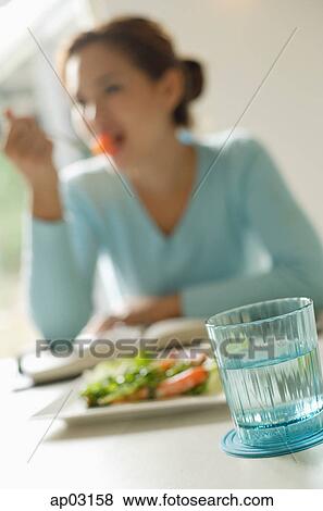 Young woman eating salad, focus on the glass of water View Large Photo Image Stock Photo - Young woman eating salad, focus on the glass of water. Fotosearch