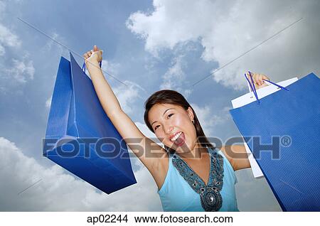 Young woman holding shopping bags, mouth open View Large Photo Image Picture - Young woman holding shopping bags, mouth open . Fotosearch