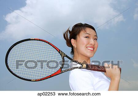 Young woman holding tennis racket over shoulder, smiling at camera View Large Photo Image Stock Image - Young woman holding tennis racket over shoulder, smiling at camera . Fotosearch