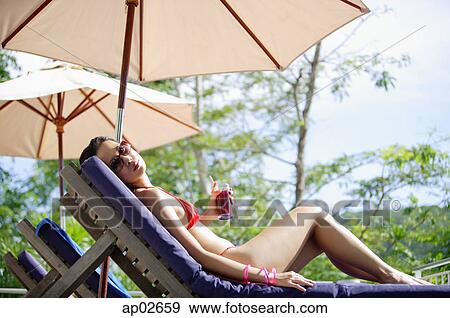 Stock Photo - Young woman in bikini, lying on deck chair, looking over shoulder . Fotosearch