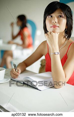 Young woman in cafe, writing in notebook, hand on chin View Large Photo Image Stock Image - Young woman in cafe, writing in notebook, hand on chin . Fotosearch