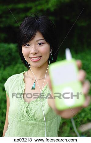 Young woman listening to mp3 player, holding it out to camera, selective focus View Large Photo Image Stock Photo - Young woman listening to mp3 player, holding it out to camera, selective focus . Fotosearch