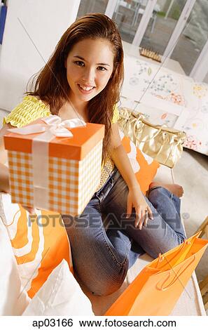 Stock Photograph - Young woman sitting, holding gift box out to camera . Fotosearch