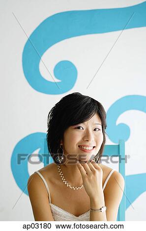 Young woman sitting on chair, looking at camera, hand on chin View Large Photo Image Stock Image - Young woman sitting on chair, looking at camera, hand on chin . Fotosearch