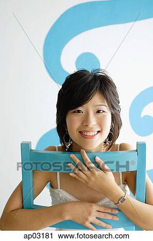 Young woman sitting on chair, smiling at camera View Large Photo Image Stock Image - Young woman sitting on chair, smiling at camera . Fotosearch