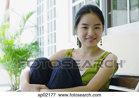 Young woman smiling at camera, hugging knees View Large Photo Image Stock Photo - Young woman smiling at camera, hugging knees . Fotosearch