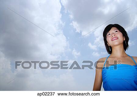 Young woman standing, looking away, low angle view View Large Photo Image Stock Photo - Young woman standing, looking away, low angle view . Fotosearch
