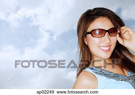 Young woman wearing sunglasses, smiling at camera View Large Photo Image Stock Photo - Young woman wearing sunglasses, smiling at camera . Fotosearch
