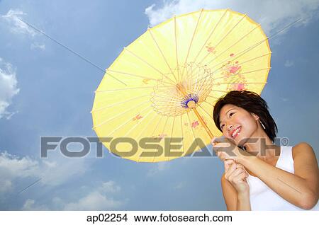 Young woman with yellow umbrella, smiling, low angle view View Large Photo Image Picture - Young woman with yellow umbrella, smiling, low angle view . Fotosearch