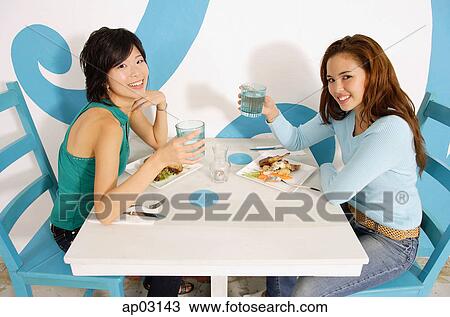 Young women having lunch in cafe, raising water glasses to camera View Large Photo Image Stock Image - Young women having lunch in cafe, raising water glasses to camera . Fotosearch