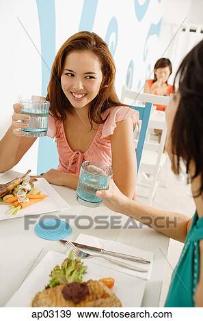 Young women in cafe, having lunch, holding glasses of water View Large Photo Image Stock Photo - Young women in cafe, having lunch, holding glasses of water. Fotosearch