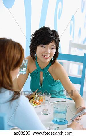 Young women in cafe, looking at mobile phone, smiling View Large Photo Image Stock Photo - Young women in cafe, looking at mobile phone, smiling . Fotosearch