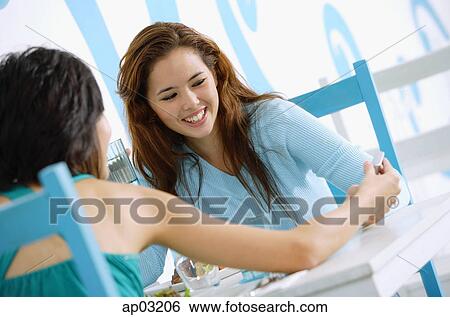 Young women in cafe, looking at mobile phone, smiling View Large Photo Image Stock Photograph - Young women in cafe, looking at mobile phone, smiling . Fotosearch