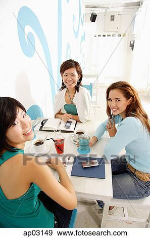 Young women sitting in cafe, looking up at camera View Large Photo Image Stock Photo - Young women sitting in cafe, looking up at camera. Fotosearch