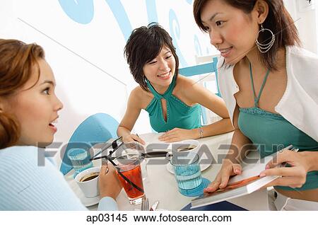 Stock Photography - Young women talking over drinks in cafe. Fotosearch
