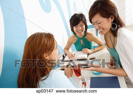 Young women talking over drinks in cafe, one woman mobile phone View Large Photo Image Stock Photo - Young women talking over drinks in cafe, one woman mobile phone. Fotosearch