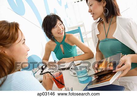 Young women talking over drinks in cafe, one woman holding book View Large Photo Image Stock Photograph - Young women talking over drinks in cafe, one woman holding book . Fotosearch