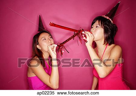 Young women wearing party hats, blowing noisemakers View Large Photo Image Stock Photography - Young women wearing party hats, blowing noisemakers . Fotosearch