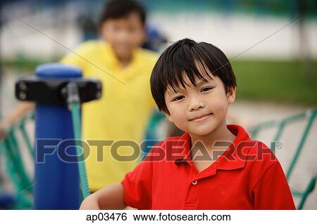 Stock Photograph - Boy in playground, looking at camera, people in the background . Fotosearch