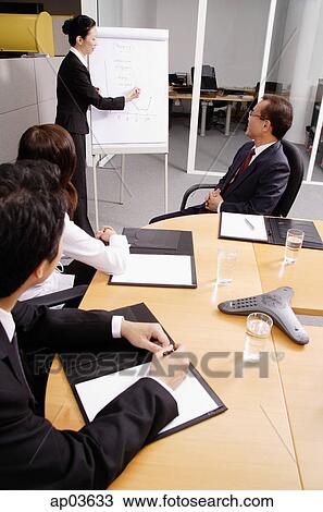 Stock Image - Business people in meeting, woman writing on flipchart . Fotosearch