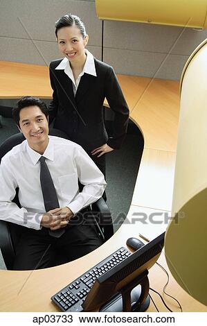 Stock Image - Businessman and woman in office cubicle, smiling at camera . Fotosearch