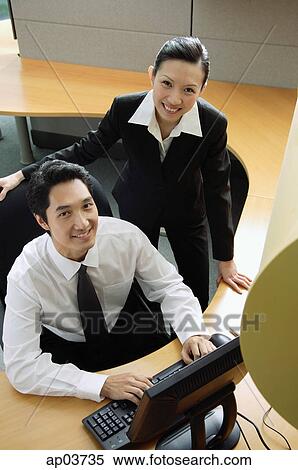 Businessman and woman in office cubicle, looking up at camera, smiling View Large Photo Image Stock Photography - Businessman and woman in office cubicle, looking up at camera, smiling. Fotosearch