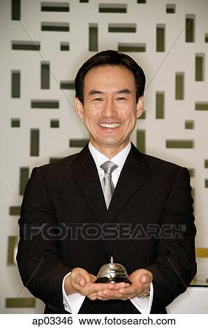 Stock Photograph - Businessman holding bell, smiling at camera. Fotosearch