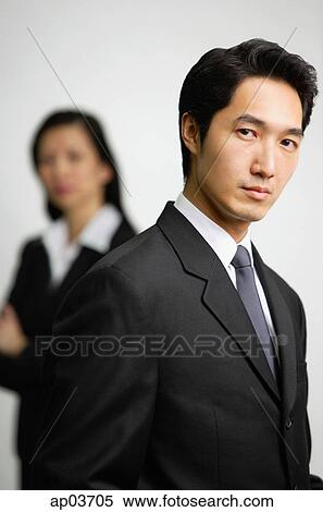 Stock Photography - Businessman looking at camera, woman in the background . Fotosearch