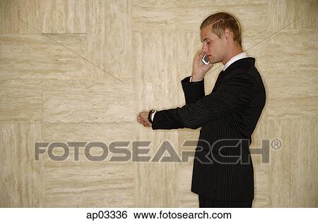 Stock Photograph - Businessman on mobile phone, looking at watch. Fotosearch